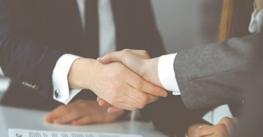 Bilinmeyen işadamı, modern ofiste iş arkadaşı ya da ortağıyla el sıkışıyor. Toplantıda iş adamları grubu