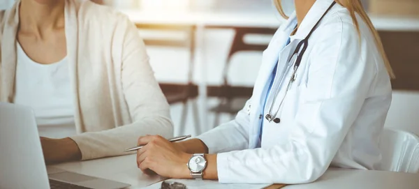 Güneşli klinikte kadın hastayla iletişim kuran kimliği belirsiz kadın doktor. Doktor tıbbi geçmişi ve sınav sonuçlarını yakından kontrol ediyor.