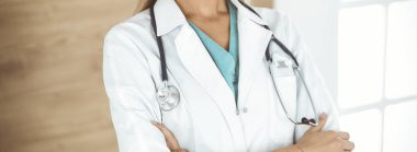 Klinikte kolları çapraz duran kimliği belirsiz kadın doktor, yakın plan. Tıp konsepti