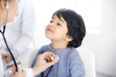 Doktor-kadın bir çocuğu steteskopla muayene ediyor. Doktor randevusunda tatlı bir Arap çocuk. Tıp konsepti