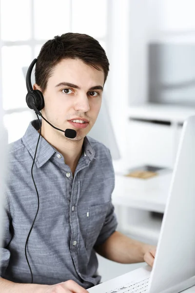 Casual dressed young man using headset and computer while talking with customers online. Call center, business concept — Stock Photo, Image