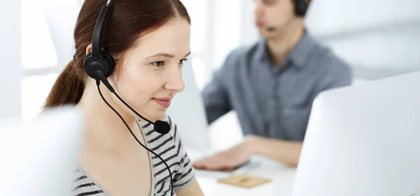 Mujer joven vestida casual usando auriculares y computadora mientras habla con los clientes en línea. Grupo de operadores en el trabajo. Call center, concepto de negocio —  Fotos de Stock