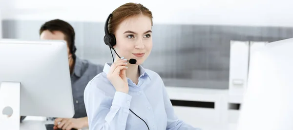 Mujer joven usando auriculares y computadora mientras habla con los clientes en línea. Grupo de operadores de centros de llamadas en el trabajo. Concepto empresarial — Foto de Stock