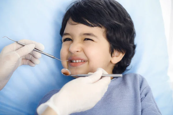 Cute chłopiec arabski siedzi na krześle dentystycznym z otwartymi ustami podczas badania doustnego z lekarzem. Odwiedzam gabinet dentystyczny. Koncepcja stomatologii — Zdjęcie stockowe