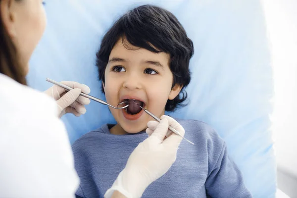 Χαριτωμένο αγόρι Άραβας κάθεται στην οδοντιατρική καρέκλα με ανοιχτό το στόμα κατά τη διάρκεια του στοματικού ελέγχου με το γιατρό. Επίσκεψη σε οδοντιατρείο. Στοματολογία έννοια — Φωτογραφία Αρχείου