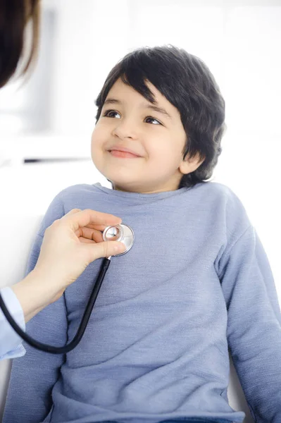 Médico-mujer examinando a un niño paciente por estetoscopio. Lindo chico árabe en la cita con el médico. Concepto de medicina —  Fotos de Stock