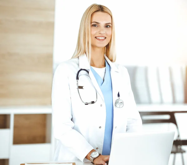 La mujer-médico controla los registros de la historia de la medicación y los resultados del examen mientras usa la computadora portátil en un hospital soleado. Concepto de medicina y salud — Foto de Stock