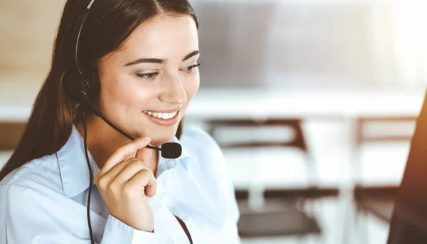 Brunette female customer service representative using headset and consulting clients online. Call center