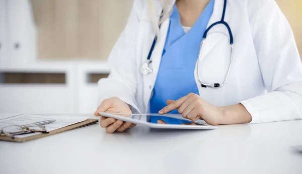 Okänd kvinnlig läkare som sitter på solig klinik och använder tablettdator, närbild. Data och bästa service inom medicin — Stockfoto