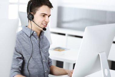 İnternette müşterilerle konuşurken kulaklık ve bilgisayar kullanan sıradan giyinmiş genç bir adam. Çağrı merkezi, iş konsepti