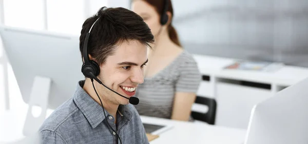 Casual dressed young man using headset and computer while talking with customers online. Group of operators at work. Call center — Stock Photo, Image