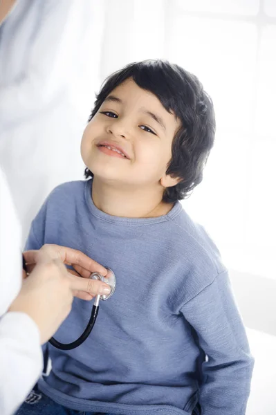 Doktorka vyšetřuje dětského pacienta stetoskopem. Roztomilý arabský chlapec na návštěvě lékaře. Koncept medicíny — Stock fotografie