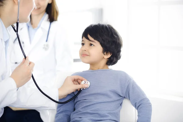 Médico-mujer examinando a un niño paciente por estetoscopio. Lindo chico árabe en la cita con el médico. Concepto de medicina —  Fotos de Stock