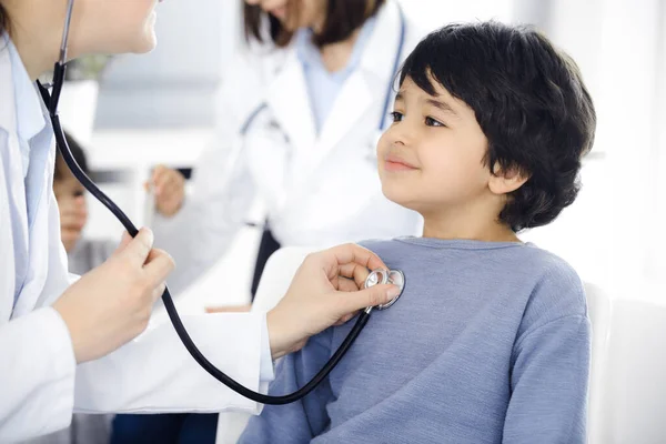 Médico-mujer examinando a un niño paciente por estetoscopio. Lindo chico árabe en la cita con el médico. Concepto de medicina — Foto de Stock