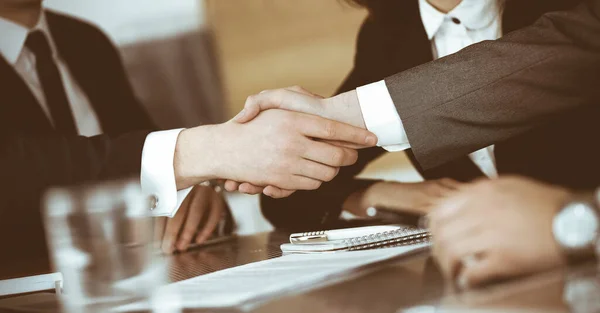 Hombre de negocios desconocido estrechando la mano con su colega o compañero por encima del escritorio de cristal en la oficina moderna, de cerca. Grupo de empresarios en la reunión — Foto de Stock