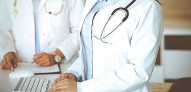 Bilinmeyen kadın doktor güneşli klinikteki resepsiyonda masaüstü bilgisayarında daktilo yazıyor. Tıp konsepti