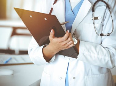 Güneşli klinikte bilinmeyen bir kadın doktor. Kadın doktor tıbbi geçmişi kontrol ediyor, yakın plan. Tıp konsepti