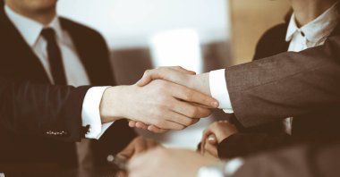 Bilinmeyen işadamı, modern ofiste iş arkadaşı ya da ortağıyla el sıkışıyor. Toplantıda iş adamları grubu