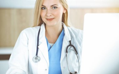 Güneşli klinikte masa başında oturan kadın doktor. Sarışın, neşeli doktor yardıma hazır.