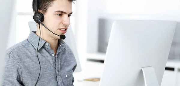 Casual dressed young man using headset and computer while talking with customers online. Call center, business concept — Stock Photo, Image