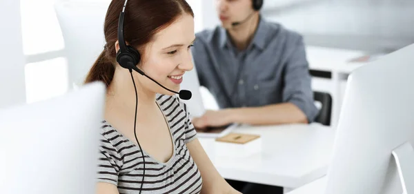 Mujer joven vestida casual usando auriculares y computadora mientras habla con los clientes en línea. Grupo de operadores en el trabajo. Call center, concepto de negocio —  Fotos de Stock