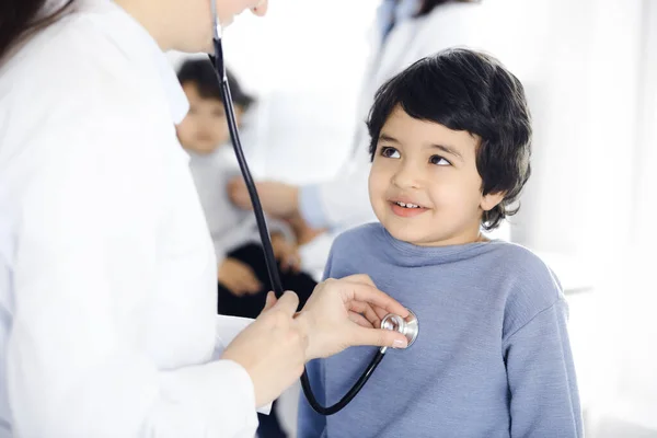 Dokter-vrouw die een kindpatiënt onderzoekt met stethoscoop. Leuke Arabische jongen en zijn broer op afspraak bij de dokter. Geneesmiddelenconcept — Stockfoto