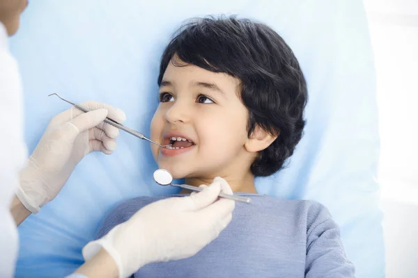 Cute chłopiec arabski siedzi na krześle dentystycznym z otwartymi ustami podczas badania doustnego z lekarzem. Odwiedzam gabinet dentystyczny. Koncepcja stomatologii — Zdjęcie stockowe