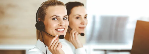 Blond female customer service representative is consulting clients online using headset in sunny office. Call center concept — Stock Photo, Image