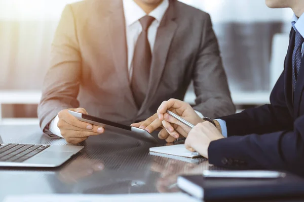 Hombre de negocios desconocido que utiliza la computadora de la tableta y el trabajo junto con su colega mientras se sienta en el escritorio de cristal en la oficina moderna. Trabajo en equipo y concepto de asociación — Foto de Stock