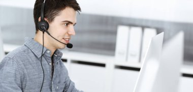 İnternette müşterilerle konuşurken kulaklık ve bilgisayar kullanan sıradan giyinmiş genç bir adam. Çağrı merkezi, iş konsepti