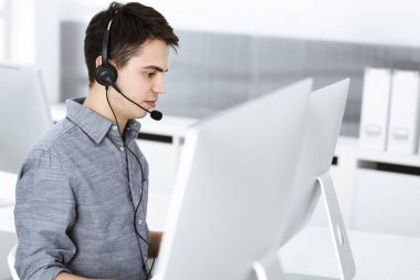 İnternette müşterilerle konuşurken kulaklık ve bilgisayar kullanan sıradan giyinmiş genç bir adam. Çağrı merkezi, iş konsepti