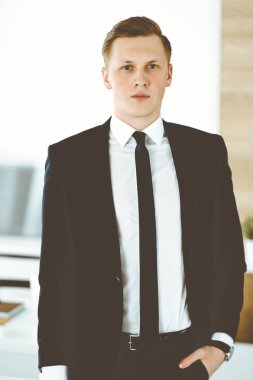 Ofisteki kameraya bakıp duran neşeli iş adamı. Genç ve başarılı girişimcinin vesikalığı