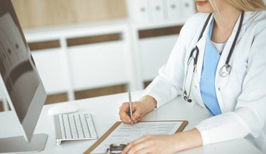 İş yerindeki bilinmeyen kadın-doktor klinikte ilaç geçmişi formunu dolduruyor, panonun yakın çekimini yapıyor.