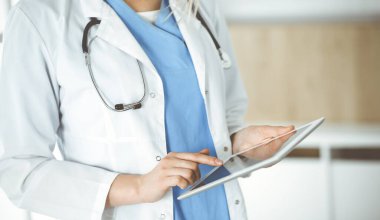 Bilinmeyen kadın doktor klinikte duruyor ve tablet bilgisayar kullanıyor, yakın plan. Veriler ve tıp ve sağlık hizmetlerindeki en iyi hizmet