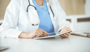 Bilinmeyen kadın doktor klinikte duruyor ve tablet bilgisayar kullanıyor, yakın plan. Veriler ve tıp ve sağlık hizmetlerindeki en iyi hizmet
