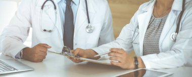 Güneşli hastane ofisindeki masada otururken tedavi sorunlarını tartışan iki bilinmeyen doktor.