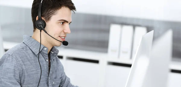 Hombre joven vestido casual usando auriculares y computadora mientras habla con los clientes en línea. Call center, concepto de negocio —  Fotos de Stock