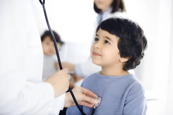 Médico-mujer examinando a un niño paciente por estetoscopio. Lindo chico árabe y su hermano en la cita con el médico. Concepto de medicina — Foto de Stock