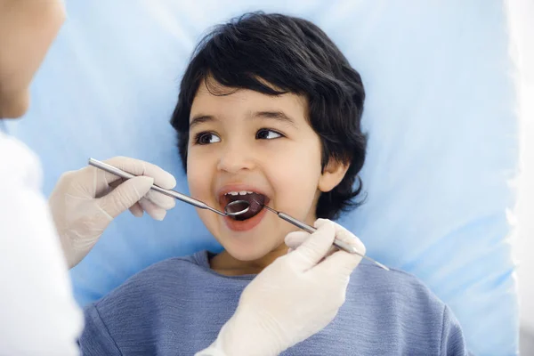 Cute arab boy sitting at dental chair with open mouth during oral checking up with doctor. Visiting dentist office. Stomatology concept — Stock Photo, Image