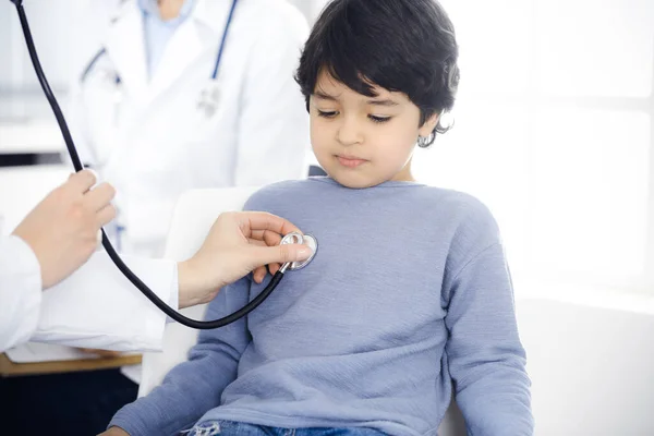 Médico-mujer examinando a un niño paciente por estetoscopio. Lindo chico árabe en la cita con el médico. Concepto de medicina —  Fotos de Stock