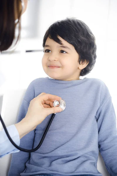 Лікар-жінка, яка вивчає пацієнта за стетоскопом. Милий арабський хлопчик за призначенням лікаря. Концепція медицини — стокове фото