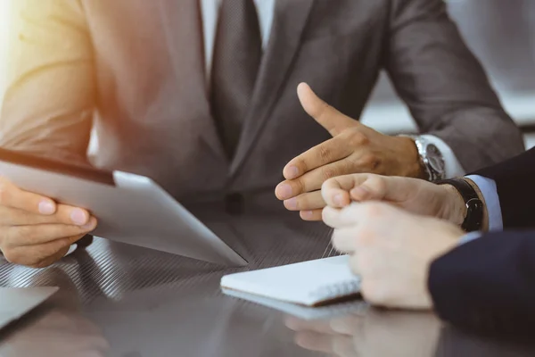 Hombre de negocios desconocido que utiliza la computadora de la tableta y el trabajo junto con su colega mientras se sienta en el escritorio de cristal en la oficina moderna. Trabajo en equipo y concepto de asociación — Foto de Stock