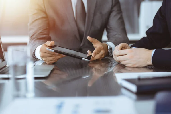 Hombre de negocios desconocido que utiliza la computadora de la tableta y el trabajo junto con su colega mientras se sienta en el escritorio de cristal en la oficina moderna. Trabajo en equipo y concepto de asociación — Foto de Stock