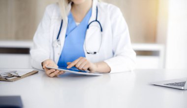 Bilinmeyen kadın doktor güneşli klinikte oturuyor ve tablet bilgisayar kullanıyor, yakın plan. Veriler ve tıptaki en iyi hizmet