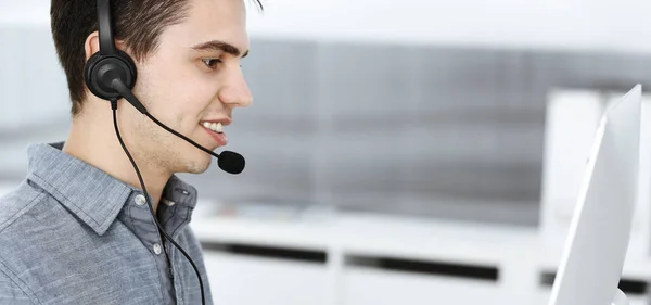 Hombre joven vestido casual usando auriculares y computadora mientras habla con los clientes en línea. Call center, concepto de negocio —  Fotos de Stock