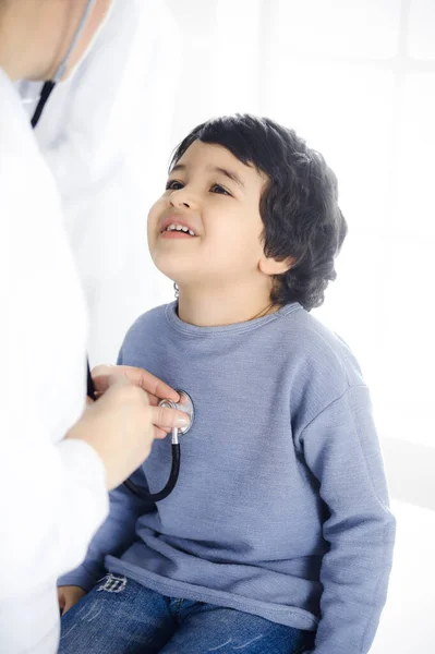 Женщина-врач осматривает ребенка стетоскопом. Милый арабский мальчик на приеме у врача. Концепция медицины — стоковое фото