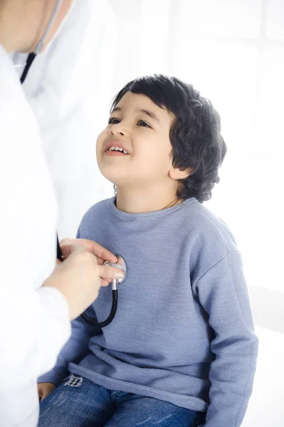 Médico-mujer examinando a un niño paciente por estetoscopio. Lindo chico árabe en la cita con el médico. Concepto de medicina —  Fotos de Stock