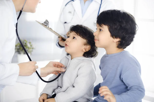 Medico-donna che esamina una paziente infantile mediante stetoscopio. Carino il bambino arabo e suo fratello su appuntamento medico. Concetto di medicina — Foto Stock