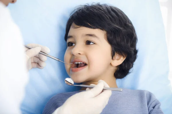 Cute arab boy sitting at dental chair with open mouth during oral checking up with doctor. Visiting dentist office. Stomatology concept — Stock Photo, Image