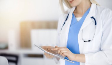 Bilinmeyen kadın doktor güneşli klinikte duruyor ve tablet bilgisayar kullanıyor, yakın plan. Veriler ve tıptaki en iyi hizmet